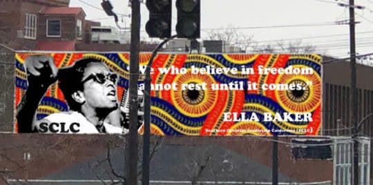 A mural on the side of the building in bright orange, yellow, purple, and blues. On the left is a black and white image of Ella Baker with her arm raised. On the right is the quote 